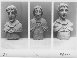 Three carved busts of men in cloaks. Photograph is in black and white, background is plain.